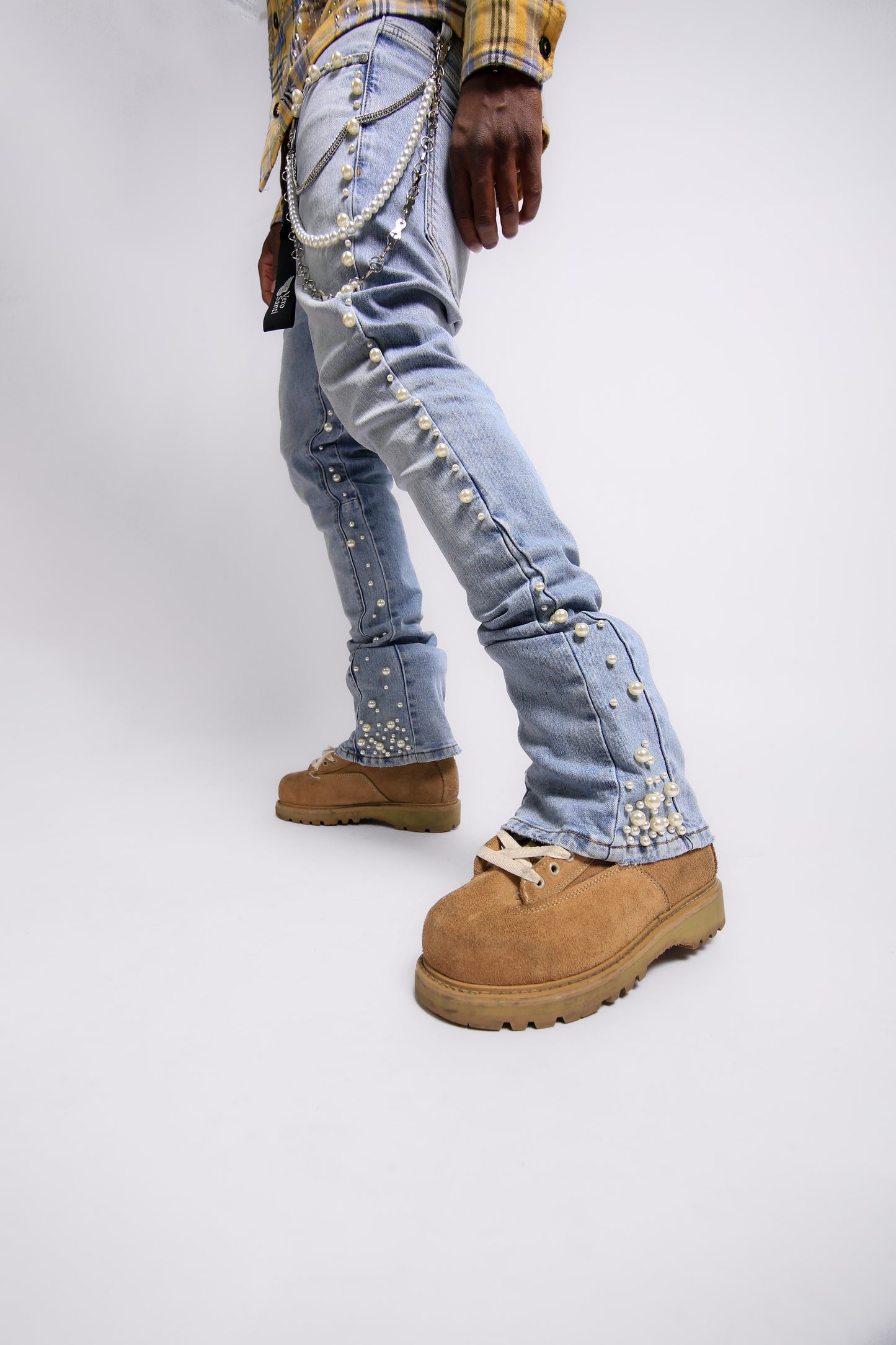 Person wearing light blue jeans with decorative elements and brown boots on a white background