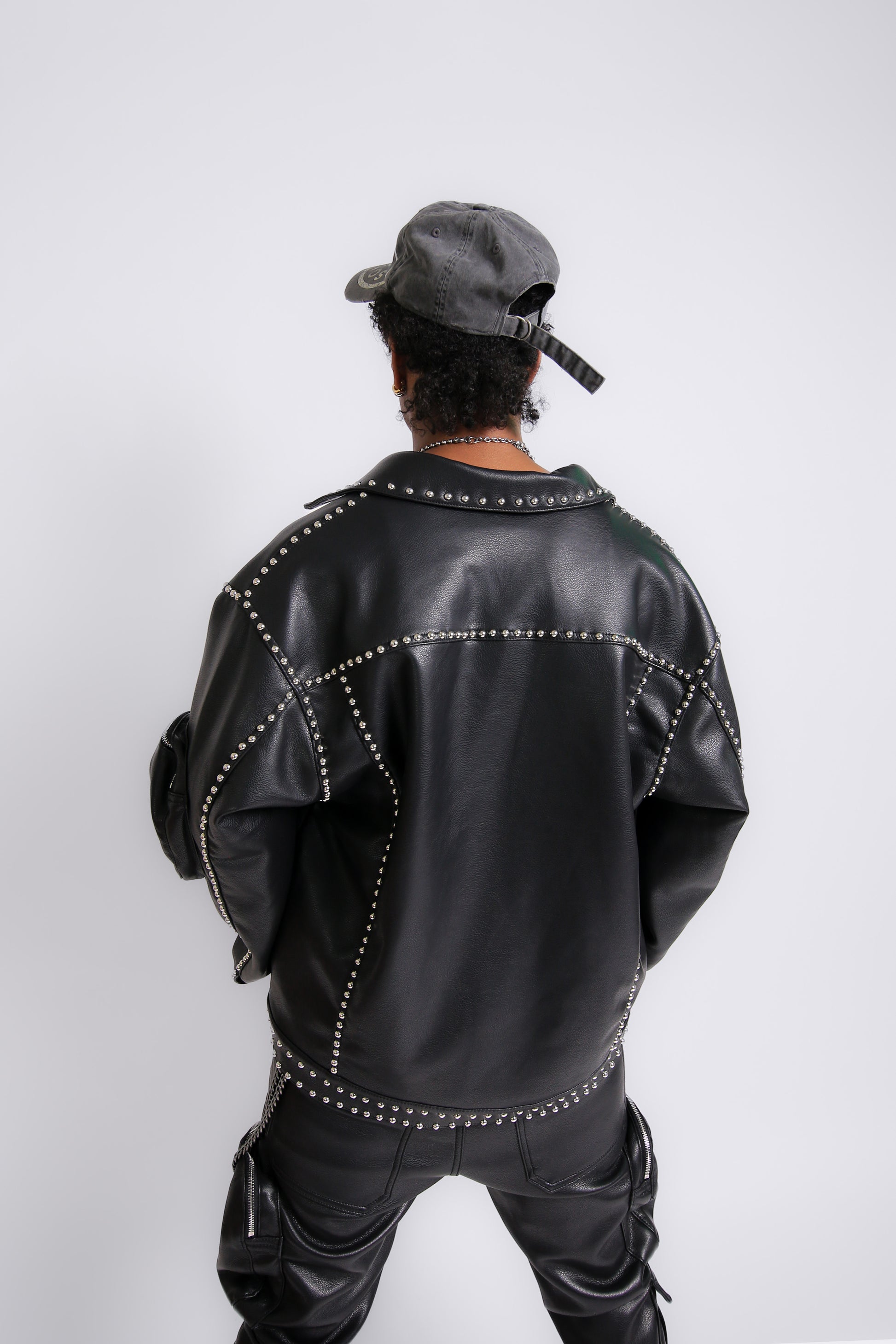 Person wearing a black leather jacket with studs and pants on a white background