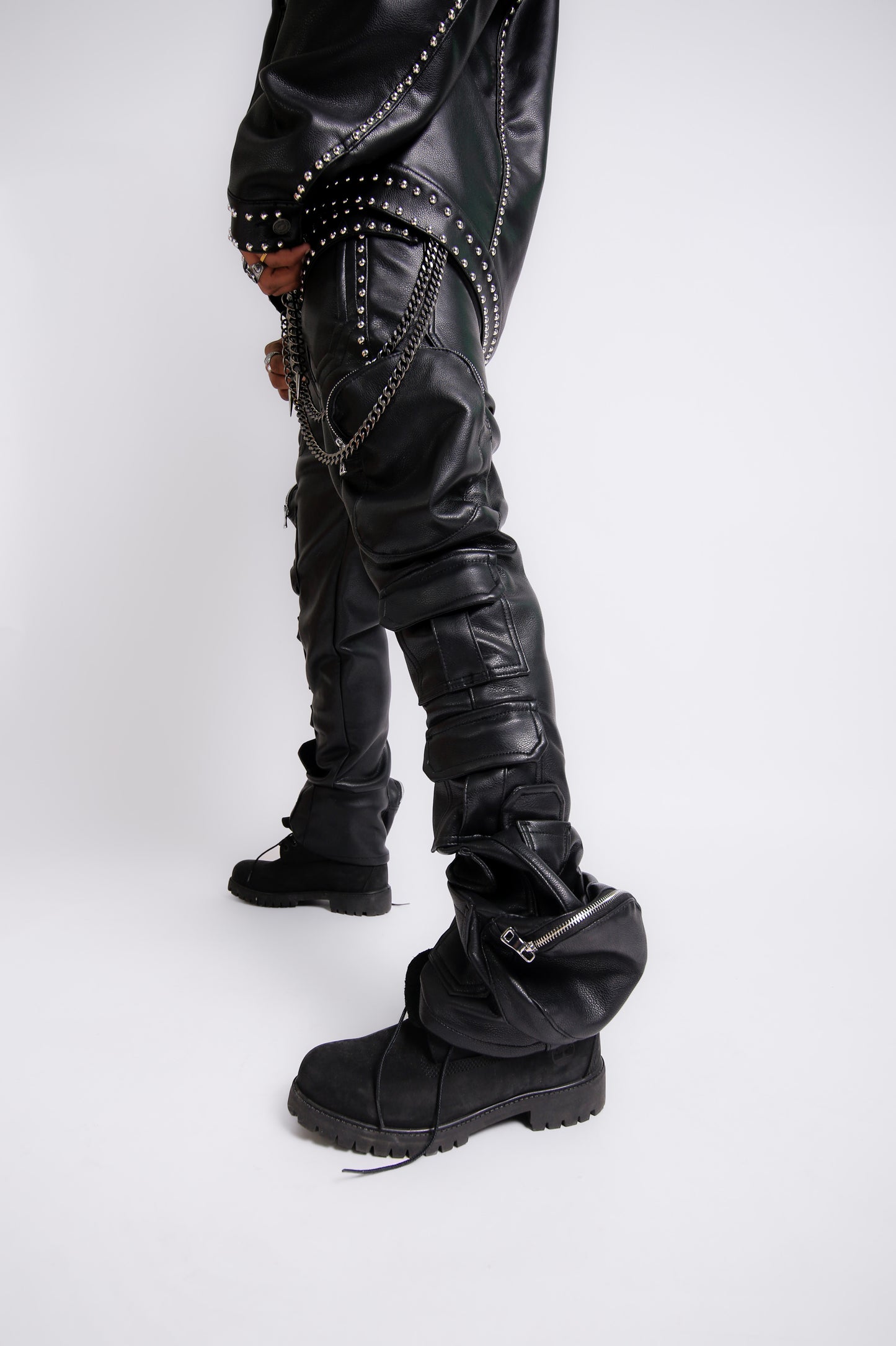 Person wearing black leather pants with studs and zippers, and black boots on a white background