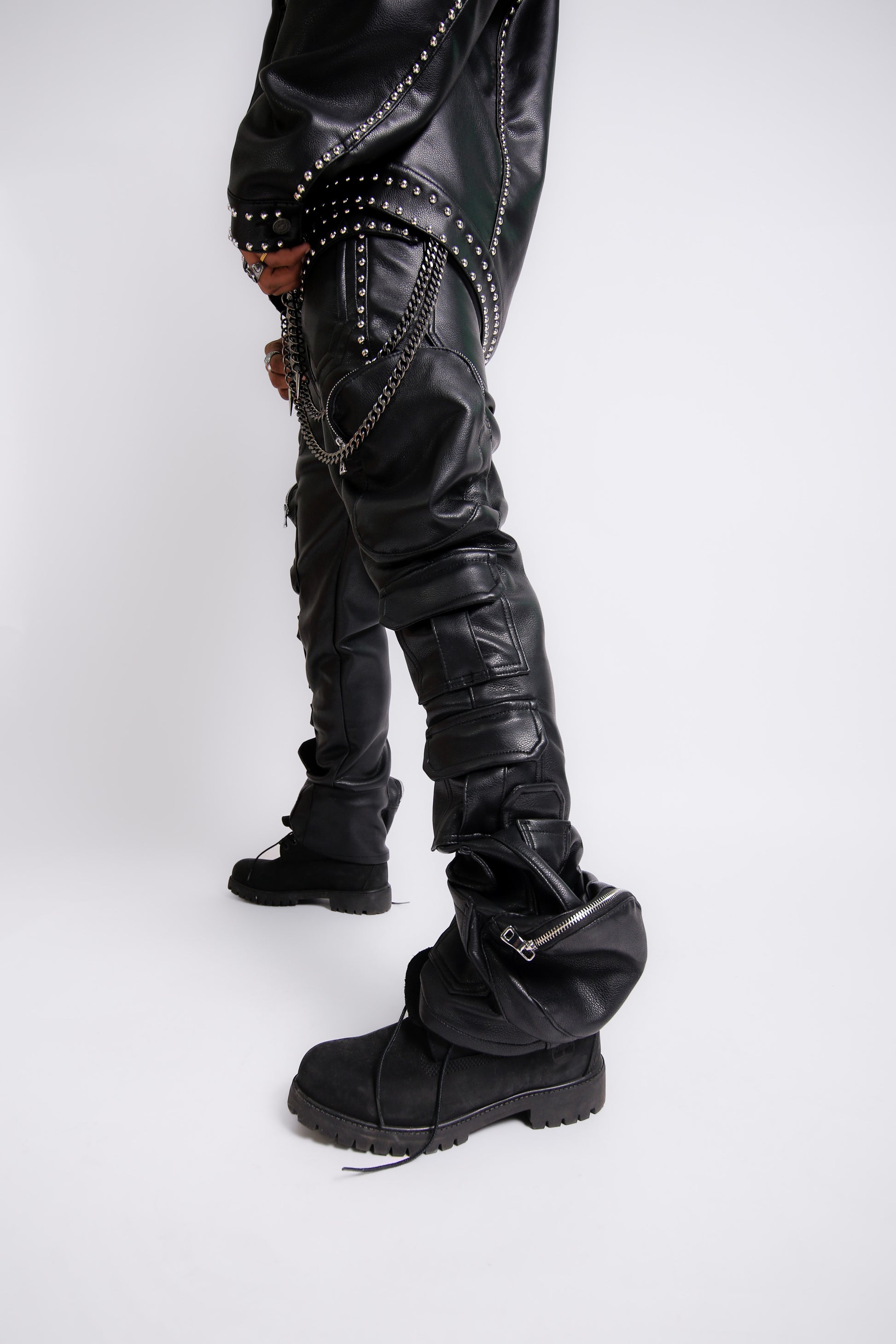 Person wearing black leather pants with studs and zippers, and black boots on a white background