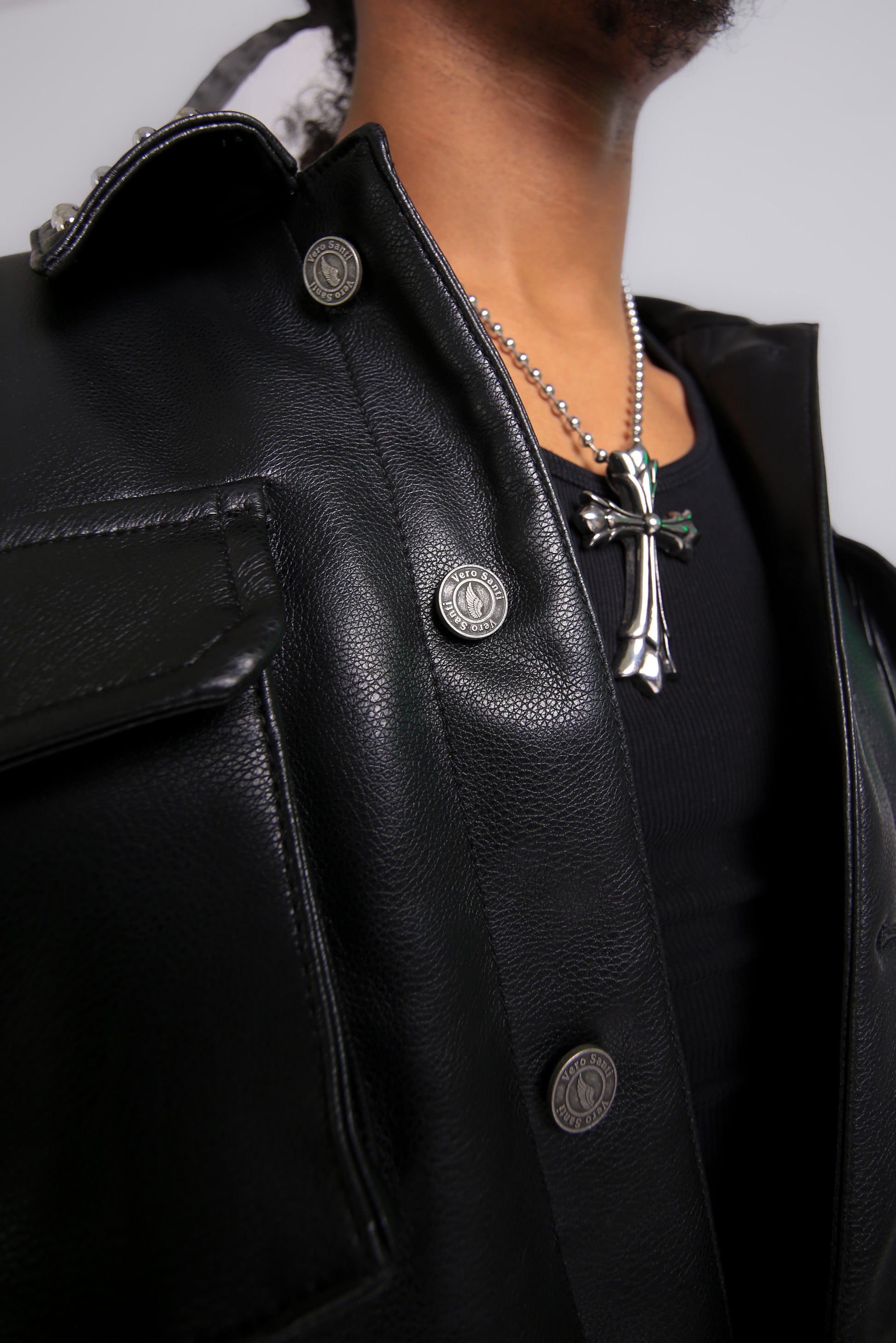 Close-up of a person wearing a black leather jacket with a cross necklace.