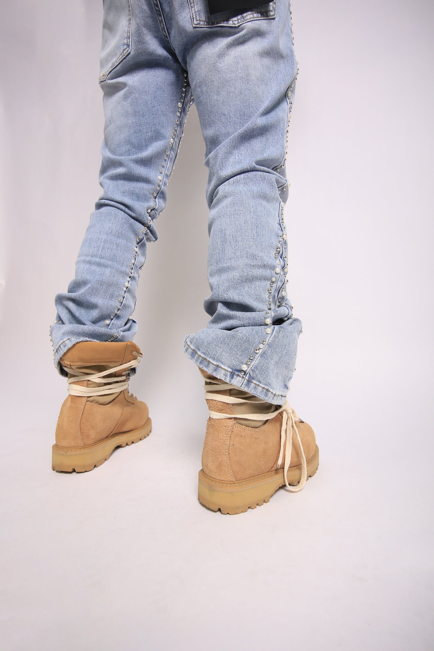 Light blue jeans with rolled-up cuffs worn with beige boots on a plain background