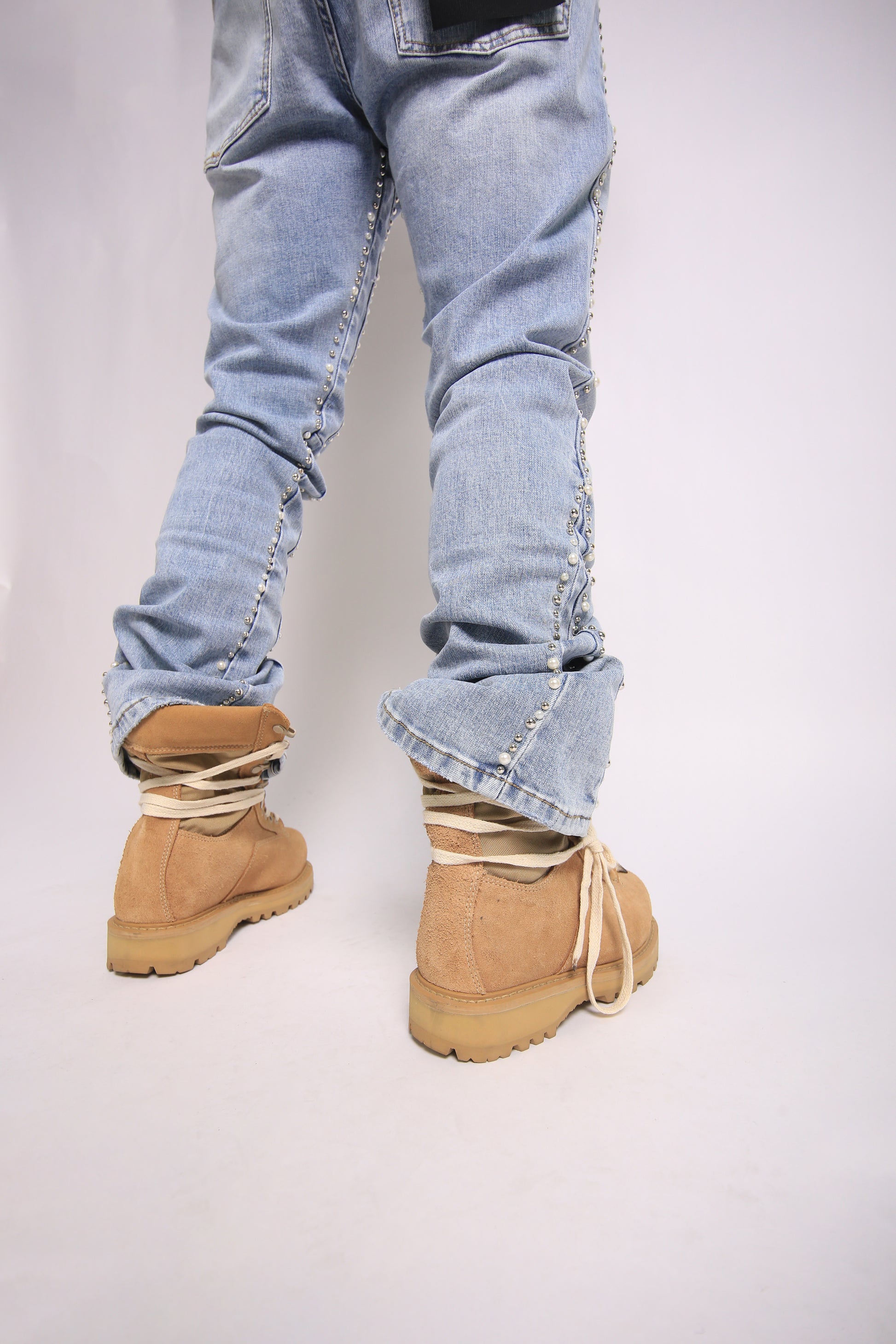 Light blue jeans with rolled-up cuffs worn with beige boots on a plain background