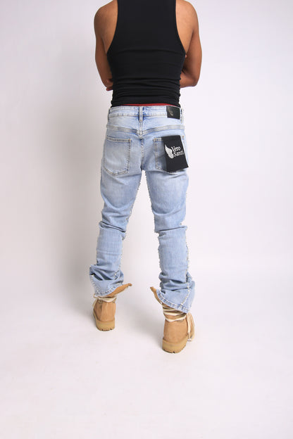 Person wearing light blue jeans with a patch on the back pocket against a white background