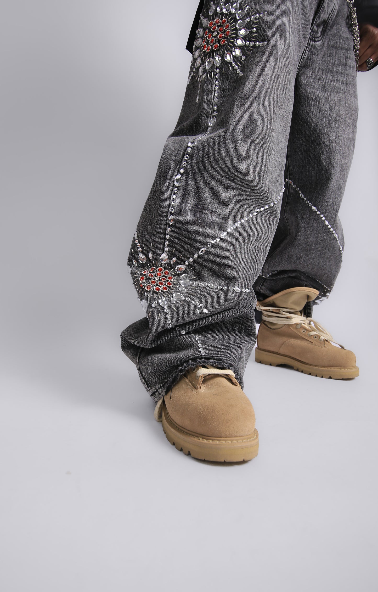 Gray jeans with decorative elements and tan boots on a plain background