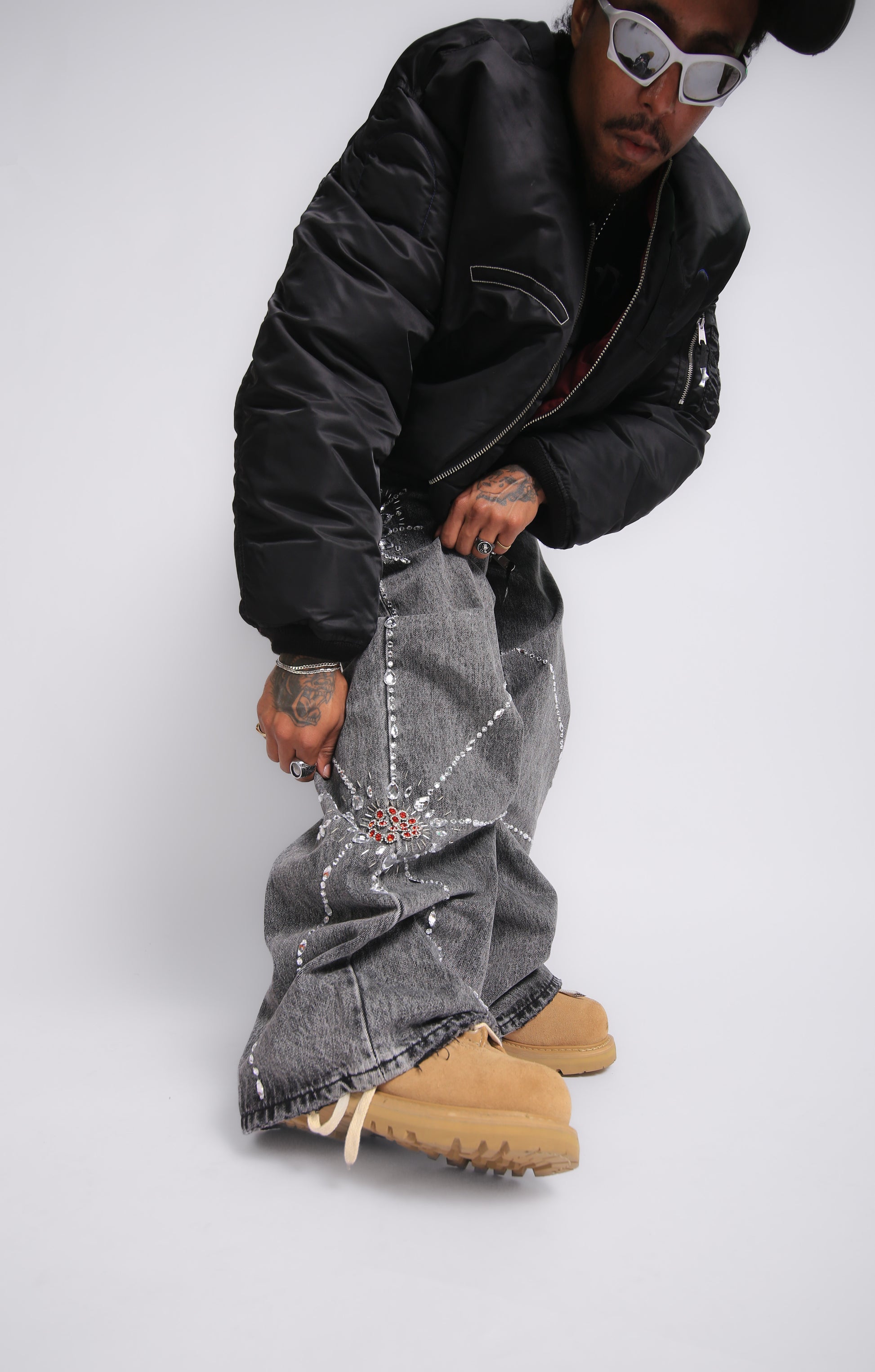 Person wearing a black jacket, gray jeans, and tan boots on a white background