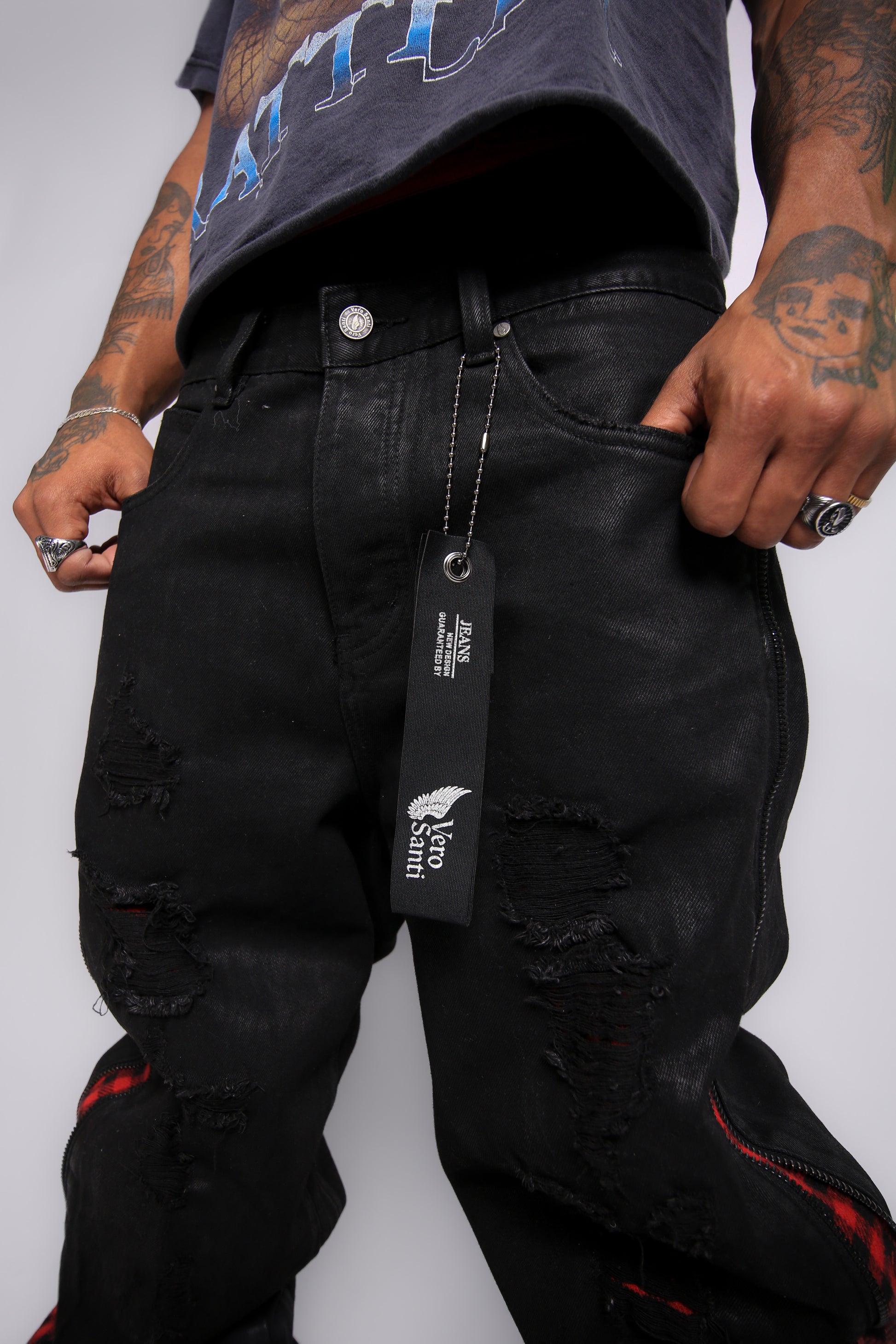 Person wearing black distressed jeans with a brand tag, on a plain background