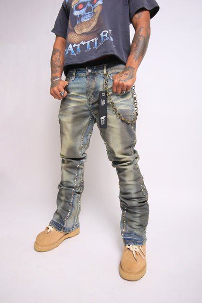 Person wearing distressed jeans with patches and a chain, standing against a plain background
