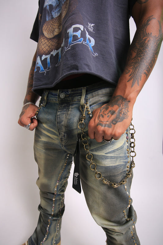 Person wearing a dark t-shirt with visible branding and distressed jeans with chains, on a plain background.