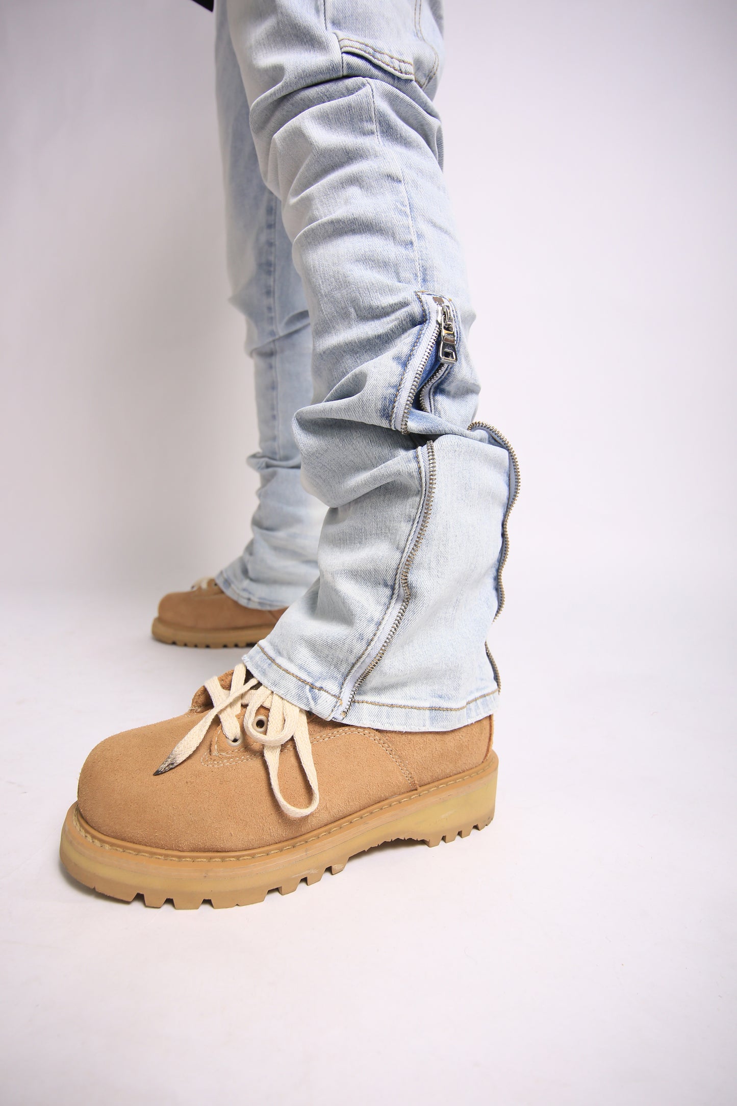 Light blue jeans with zippers and tan boots on a white background