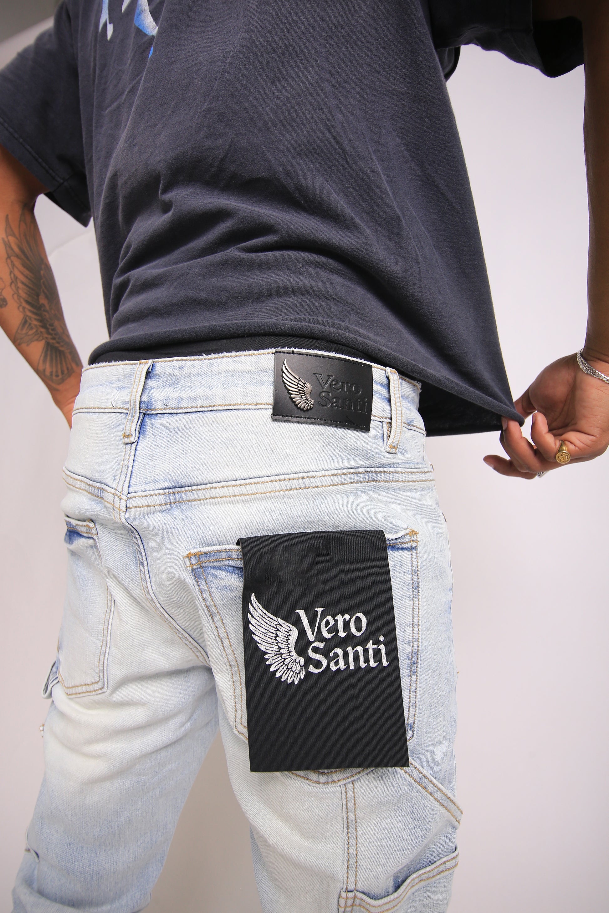 Person wearing light blue jeans with a Vero Santi patch on a plain background