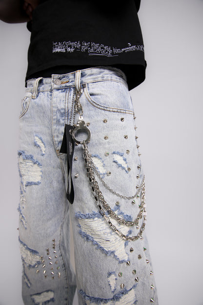 Light blue distressed jeans with silver chains and embellishments on a plain background