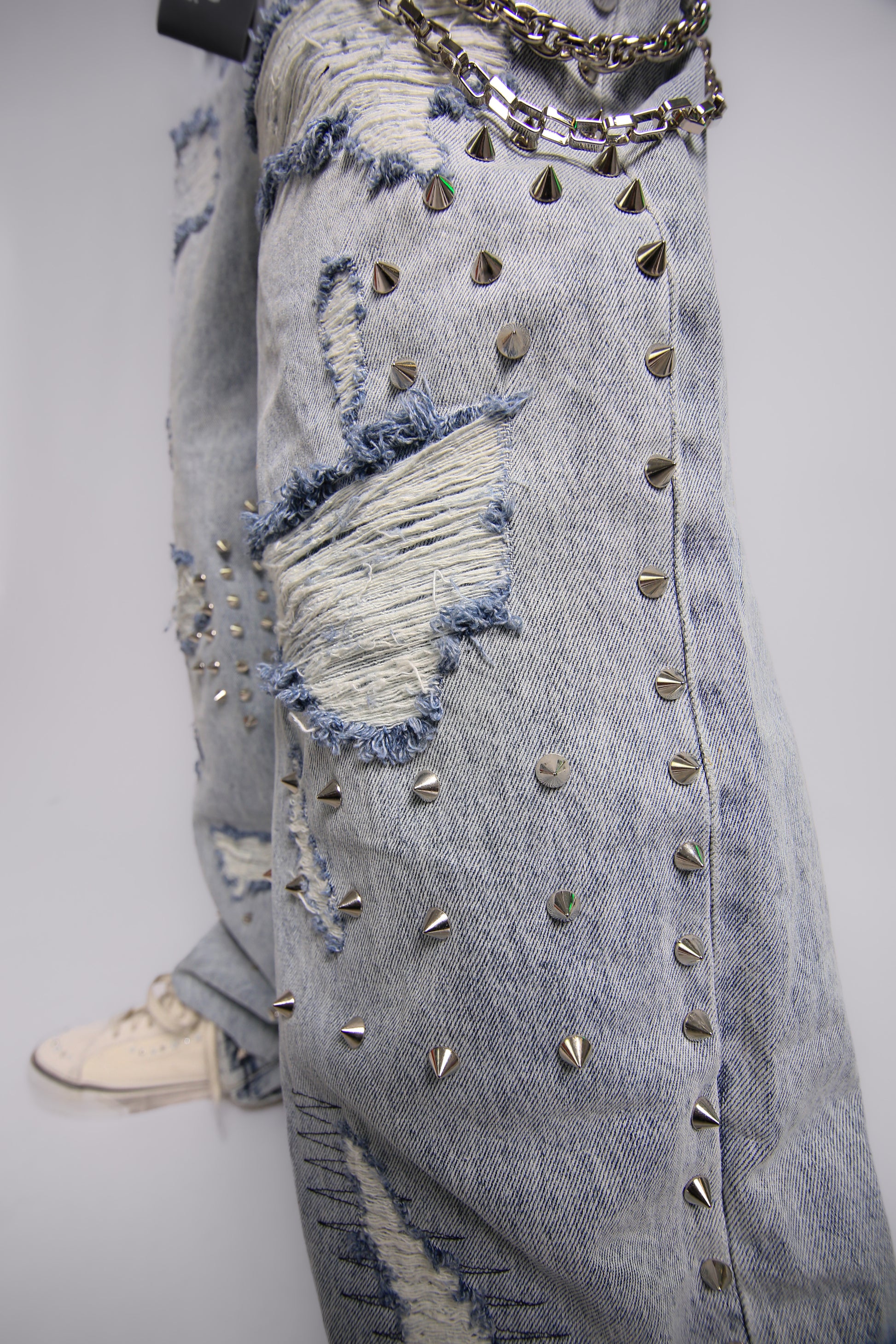 Distressed denim jeans with studs and a chain on a plain background