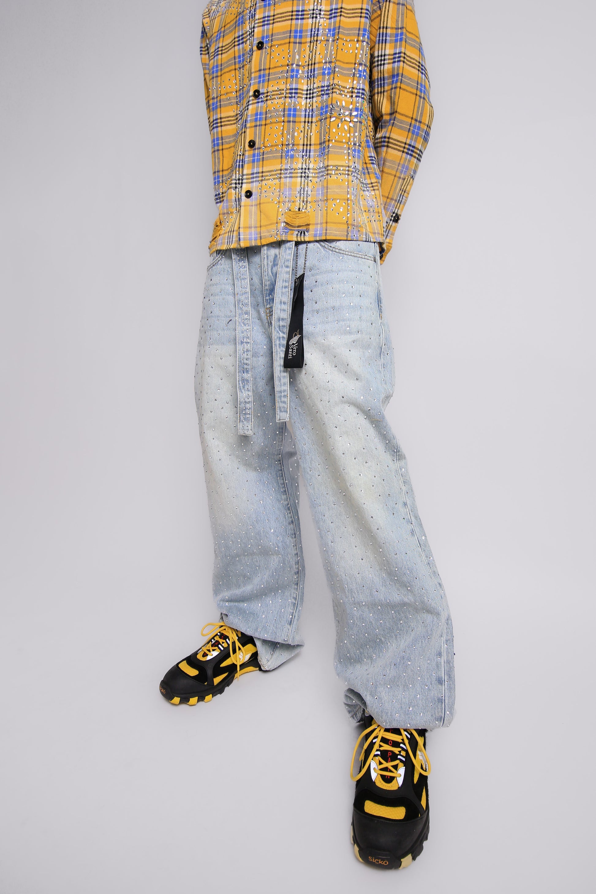 Person wearing a yellow plaid shirt, light blue jeans, and black sneakers with yellow accents on a gray background