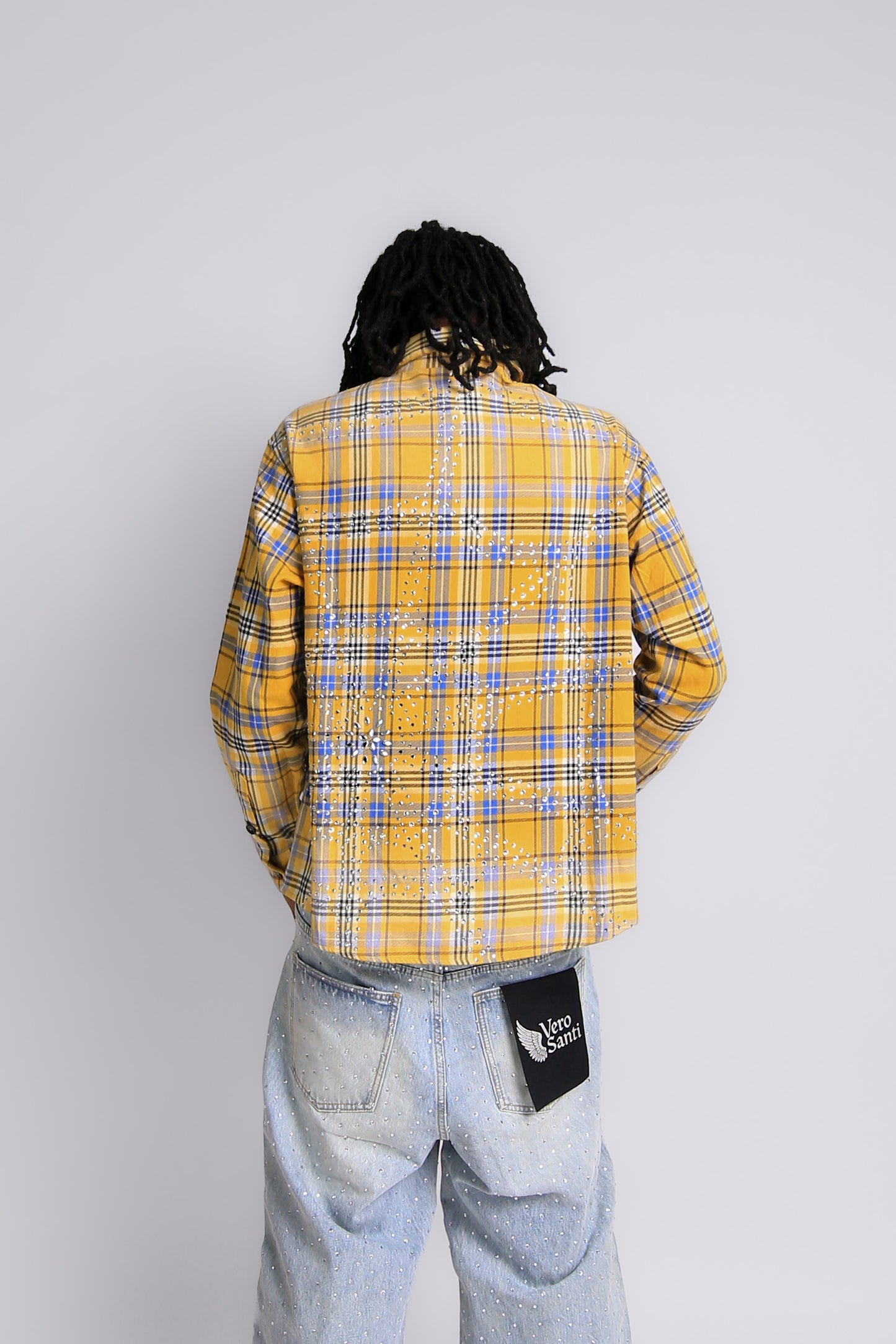 Person wearing a yellow plaid shirt and light blue jeans with a visible brand logo on a white background