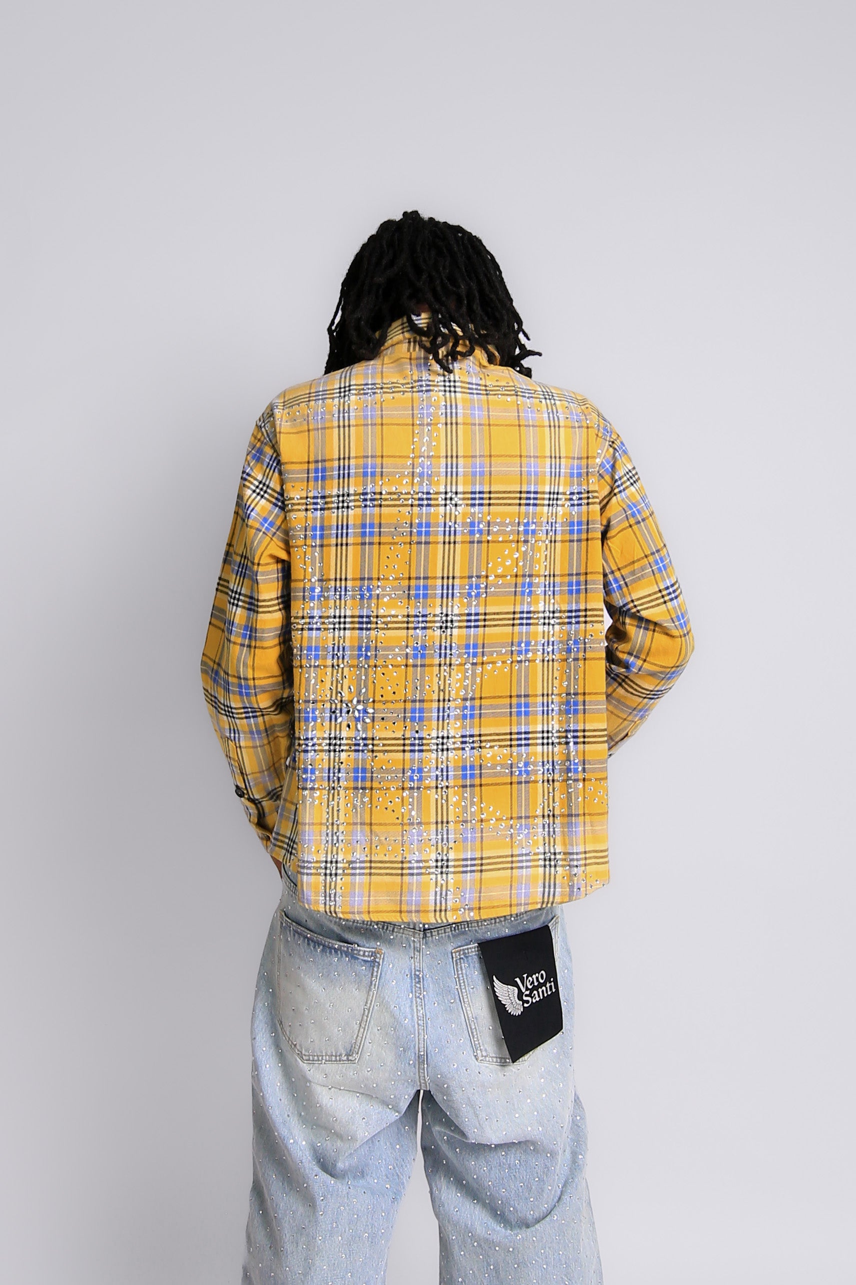 Person wearing a yellow plaid shirt and light blue jeans with a visible brand logo on a white background