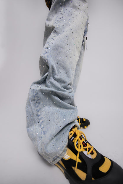 Close-up of a person wearing light blue jeans with a pattern and black and yellow shoes on a plain background