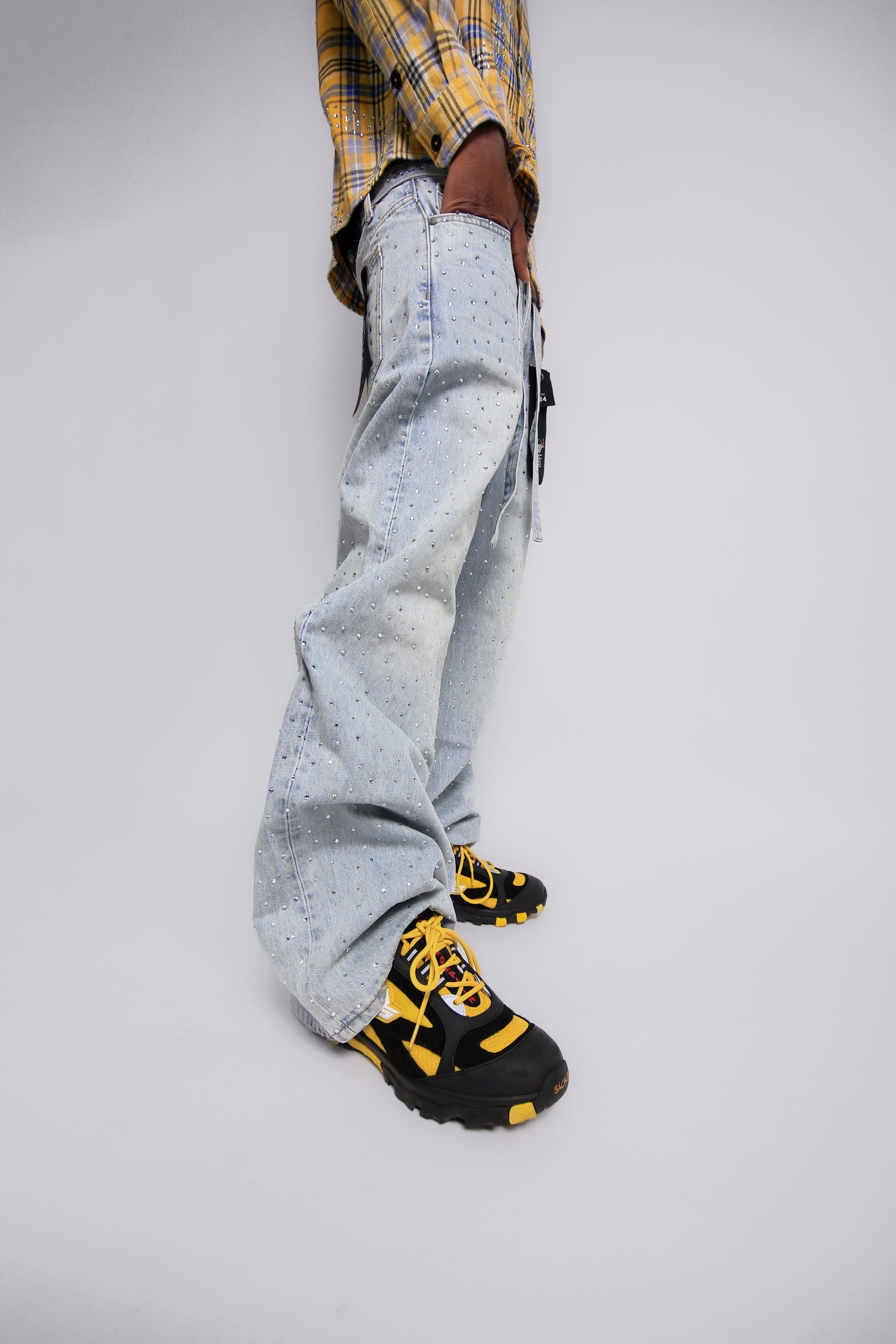 Person wearing light blue jeans and black and yellow shoes on a white background