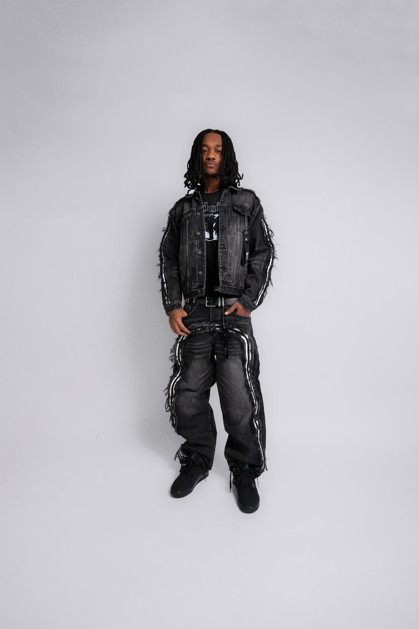 Person wearing a black denim jacket and pants on a white background