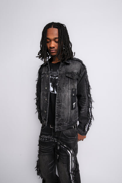 Person wearing a black denim jacket with fringe details on a white background