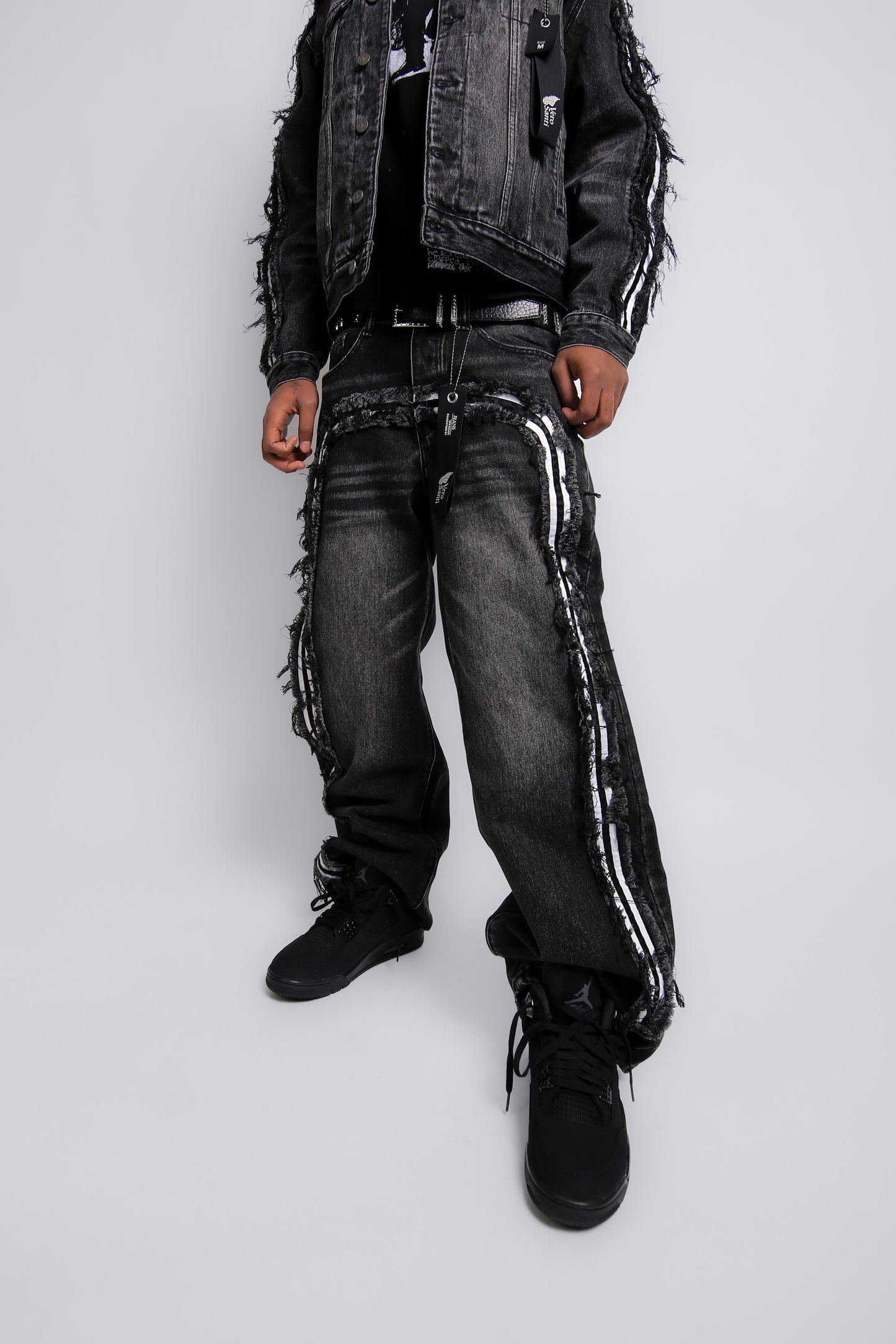 Person wearing a black distressed jacket, jeans, and boots on a white background