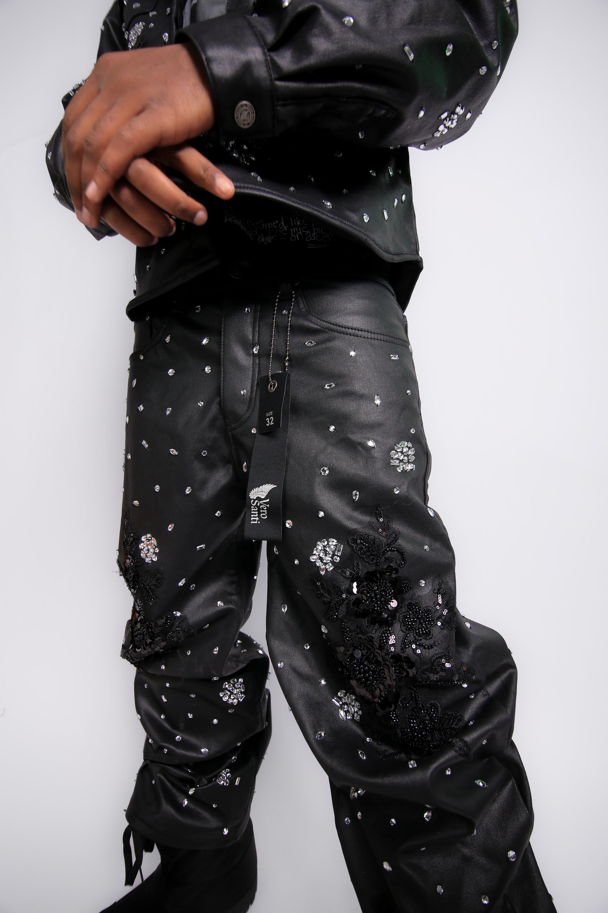 Person wearing black pants with decorative elements on a plain background