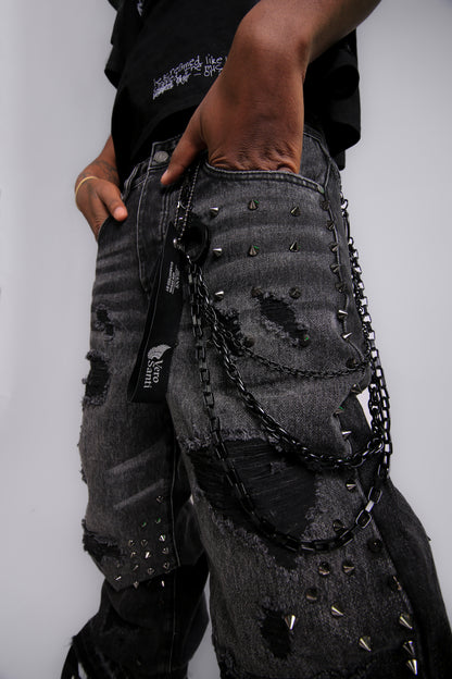 Person wearing black distressed jeans with chains on a plain background