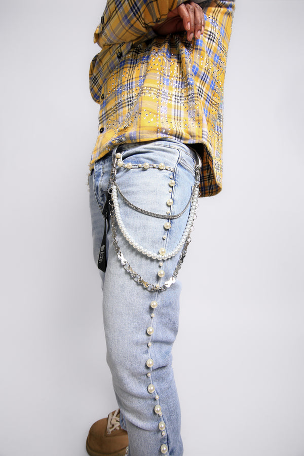 Person wearing a yellow plaid shirt and light blue jeans with decorative chains on a white background
