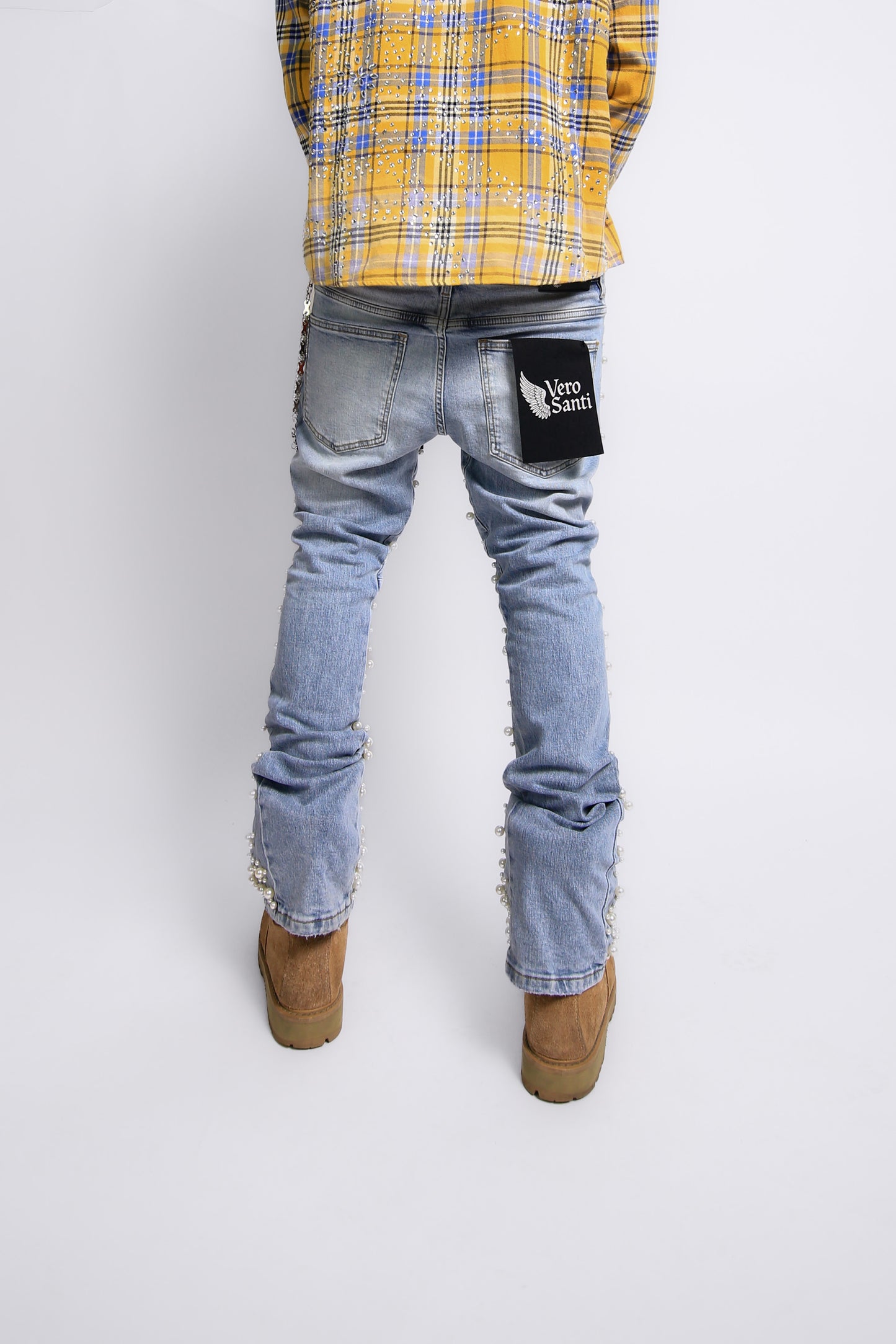 Person wearing light blue jeans with a patch, yellow plaid shirt, and brown boots on a white background